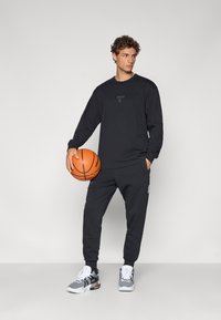 Black long-sleeve shirt with logo, matching black sweatpants, and gray and black athletic shoes. Holds a basketball. Simple design and fit.