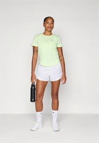 Camiseta desportiva verde clara, calções brancos, garrafa de água preta na mão, com ténis desportivos brancos e meias. Design minimalista, textura suave.