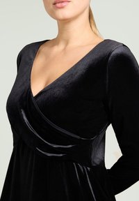 Schwarzes Samtkleid mit Wickeldesign, tiefem V-Ausschnitt, langen Ärmeln und weicher Textur, mit fließendem Rock und dezentem Glanz.