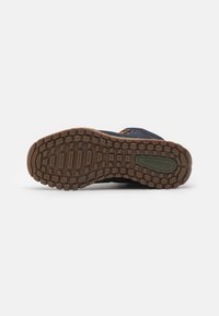 Semelle de chaussure de randonnée bleu foncé avec un caoutchouc texturé pour une meilleure adhérence. Présente une semelle extérieure marron et un accent de logo vert près du talon.