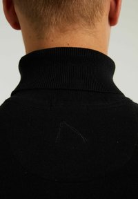 Schwarzer, gestrickter Pullover mit hohem Kragen, der eine gerippte Textur und ein unregelmäßiges Stichdetail nahe dem Kragen auf der Rückseite aufweist.