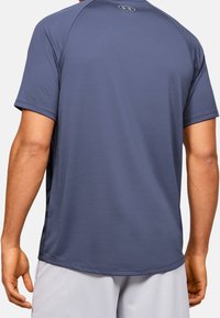 Granatowa sportowa koszulka z krótkim rękawem, wykonana z gładkiego materiału, z zaokrąglonym dekoltem i detalem z logo na plecach. Widoczny projekt bocznego panelu.