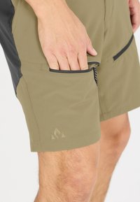 Olivgröna shorts med svarta detaljer, tillverkade av lättviktig material. Har sidofickor och en triangellogo på underbenet.