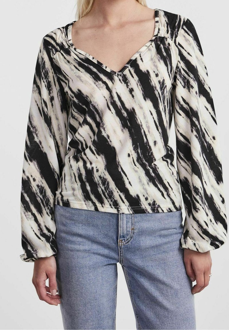 Långärmad topp i svart och krämfärgad vågmönster, med V-ringning och lätt insydda axlar, kombinerad med ljusblå jeans.