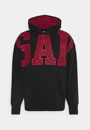 Sweat à capuche noir avec de grandes lettres rouges GAP sur la poitrine et les épaules, ornées de motifs floraux complexes à l'intérieur des lettres.