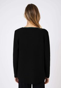 Pull en tricot noir avec une finition texturée, présentant un col rond et un intérieur à motif contrasté à l'arrière. Manches longues, coupe décontractée.