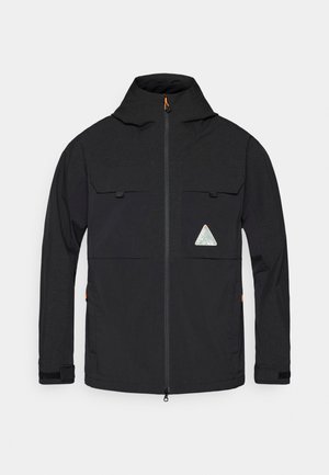 Zwarte jas met een hoge kraag, ritssluiting aan de voorkant, twee bovenzakken en een driehoekig logo op de borst; heeft een textuurstof en oranje accenten.