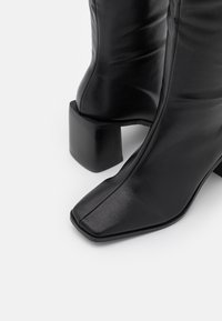 Czarne skórzane botki za kostkę o kwadratowym nosku i teksturowanym wykończeniu, z masywnym blokowym obcasem i gładką sylwetką.