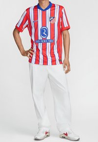 Punainen ja sininen raidoitettu urheilujuoksupaita, jossa on lyhyet hihat, V-pääntie ja logo. Yhdistetty valkoisiin housuihin ja valkoisiin lenkkareihin, joissa on punaisia korostuksia.