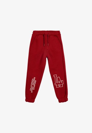 Pantalones de chándal rojos hechos de una tela suave, con una cinturilla elástica y cordones, bolsillos laterales y acentos gráficos impresos en blanco.