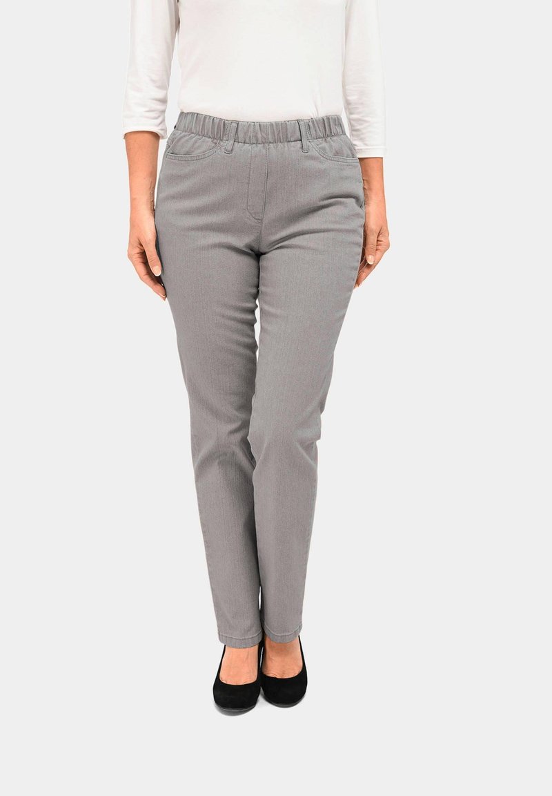 Graue Stretchhose mit einem elastischen Bund und zwei Fronttaschen, schmal geschnitten und mit subtiler vertikaler Textur. Getragen mit schwarzen Schuhen.