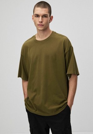 Olive green oversize t-shirt wykonany z bawełny, z krótkimi rękawami, okrągłym dekoltem i subtelnym haftem na piersi.