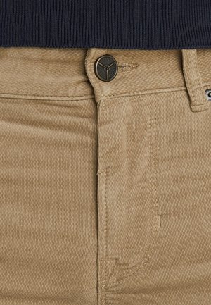 Beige corduroy broek met een gestructureerd oppervlak, voorzien van een bruine metalen knoop bij de taille en zichtbare stiksels langs de randen.