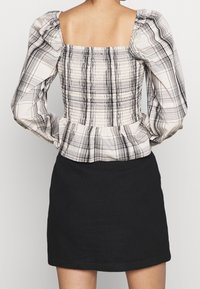 Valkea ja musta ruudullinen paita puffihihoilla, smokkitaustalla ja röyhelöhelmalla, yhdistettynä tiukkaan mustaan hameeseen.