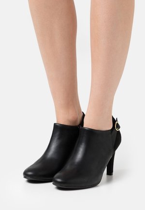 Černé kožené kotníkové boty s špičatými špičkami, bočním zipem a zlatým akcentem na podpatku. Úzké, vysoké jehlové podpatky. Hladká textura.