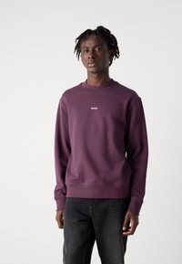 Sudadera púrpura hecha de una mezcla de algodón, con un cuello redondo, puños y dobladillo acanalados, y un pequeño logo "BOSS" en el pecho.