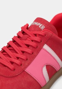Felrode sneaker met roze en lichtroze zijstrepen, rode veters en witte "CAMPER"-branding op de tong.