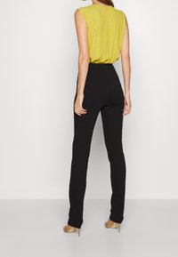 Haut sans manches jaune avec un motif texturé, associé à un pantalon noir ajusté et des chaussures à talons hauts couleur nude. Silhouette simple et moderne.