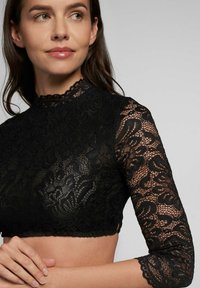 Zwarte kanten crop top met lange mouwen, voorzien van een hoge halslijn en gezette manchetten, die ingewikkelde bloemmotieven en een doorschijnende textuur toont.