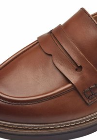 Mocassin en cuir marron avec couture mocassin, bride classique sur le dessus et construction soignée de la semelle sur le bord.