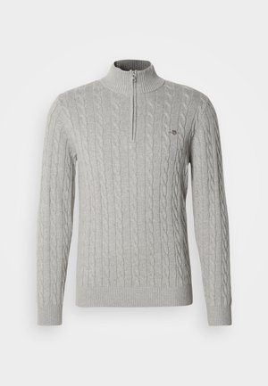 Szary sweter z dzianiny o splocie warkoczowym, z wysokim kołnierzem i półzamkiem. Charakteryzuje się teksturowanymi wzorami oraz ściągaczami na mankietach i dole, zapewniającymi dopasowanie.