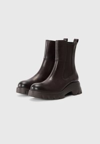 Brown leather ankle boots with a smooth finish, elastic side panels, and a chunky sole featuring deep grooves for traction.