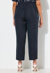 Marinblå strukturerade byxor med avslappnad passform och elastisk midja, med två bakfickor och formade fållar, kombinerade med vita klackar.