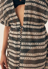 Brązowy i kremowy kimono w paski o luźnym kroju, wykonane z materiału o otwartym splocie. Posiada zapięcie na sznurek oraz kwiatowe wzory na całej powierzchni.