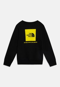Melnā sporta krekla ar apaļu kaklu. Aizmugurē ir liels dzeltena kvadrāta logo ar tekstu "THE NORTH FACE" un "NEVER STOP EXPLORING".