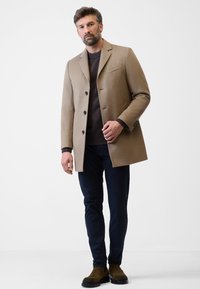 Beige ullkappa med en strukturerad design, enfärgad knappslå och en slim fit, kombinerad med mörkblå byxor och bruna mockastövlar.