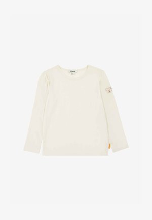 Camiseta para niño pequeño de manga larga color crema con cuello redondo, pequeño parche de oso de peluche en la manga izquierda y etiqueta de marca amarilla en el dobladillo.