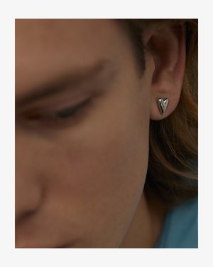 Silver heart-shaped earring against skin, featuring a smooth, polished texture. Close-up view emphasizes the design and shape.