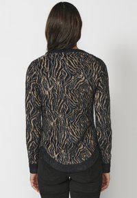 Suéter negro y beige con un patrón texturizado y ondulado, que cuenta con mangas largas, un dobladillo redondeado y un acabado de tela suave.