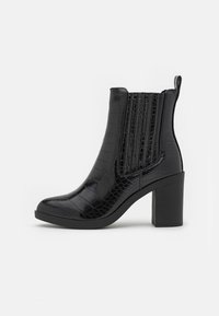 Bottines noires à talon, avec une texture crocodile brillante, bout rond et panneaux latéraux élastiques. Elles disposent d'un talon épais et d'une languette à l'arrière.