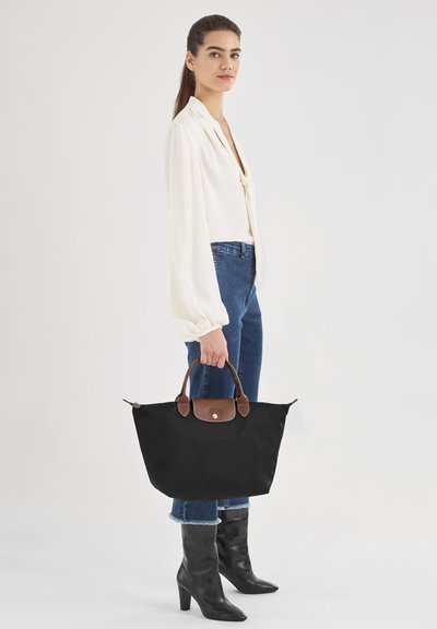Schwarze Nylon-Shopper-Tasche mit braunen Lederakzenten, ausgestattet mit zwei oberen Tragegriffen, einem Druckknopfverschluss und einer Fronttasche. Stilvolles, praktisches Design.