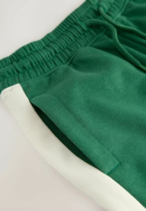 Grüne Baumwollshorts mit einem elastischen Bund, versehen mit einem weißen Seitenpanel. Der Stoff ist weich mit einer glatten Textur.
