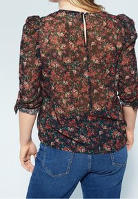 Durchsichtige Blumenbluse mit dunklem Hintergrund, die mit kleinen roten und grünen Blumen verziert ist, Puffärmeln und einem Schlüssellochverschluss auf der Rückseite.