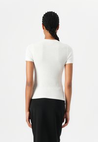 Kortærmet hvid top med en tekstureret, ribbet design. Tætsiddende pasform med round neckline og en ren afslutning ved kanten.
