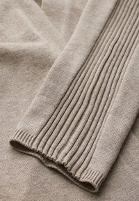 Beiger gestrickter Pullover mit strukturiertem Rippdesign an den Ärmeln, weichem Stoff und sauberem Rippabschluss am Saum. Dezente Farbvariationen im gesamten Stück.