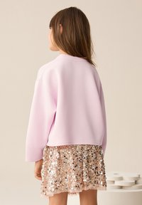 Pink cropped sweatshirt made of soft material, paired with a shiny, sequined rose gold skirt. Smooth texture, relaxed fit, subtle gleam.