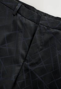 Black fabric with a textured geometric pattern in dark blue. Tailored design featuring a straight cut and discreet stitching details.