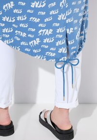 Blå t-shirt med vit "STAR" tryck, med en rynkad nederdel och blå dragsko. Återförenad med vita uppvikta byxor och svarta plattformssandaler.