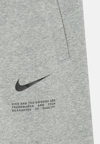 Pelēks džemperis ar melnu Nike swoosh logotipu un tekstu zem tā, izgatavots no mīkstas auduma ar gludu tekstūru un kabatām sānos.