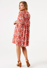 Vestido de flores rojas con mangas 3/4, cintura ceñida y falda acampanada. Llevado con sandalias de tacón cuadrado marrones.