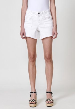 White denim shorts with frayed hem and braided detailing on the waistband. Paired with black and beige strappy platform sandals.