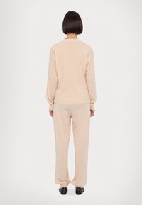 Conjunto de suéter e calças em bege claro, feito de um tecido macio. O suéter tem um corte descontraído com ombros caídos; as calças têm punhos elásticos.