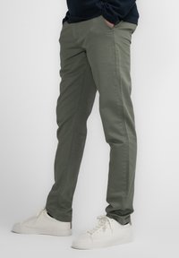 Olive green cotton pants with a slim fit, featuring side pockets and fine stitching. Paired with white sneakers.