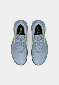 Svetlo sivi atletski čevlji s teksturiranim zgornjim delom, ki vključujejo rumene poudarke, klasično vezanje in oblazinjen podplat. Pogruntano z vrha.