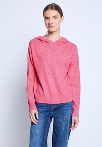 Różowa bluza z kapturem o teksturowanym wykończeniu, z regulowanym kapturem, ściągaczami na rękawach i krótkim krojem, zestawiona z niebieskimi spodniami dzwonami.