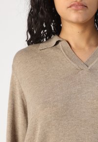 Maglione lavorato a maglia beige con scollo a V e colletto. Presenta una texture morbida e un design leggero.